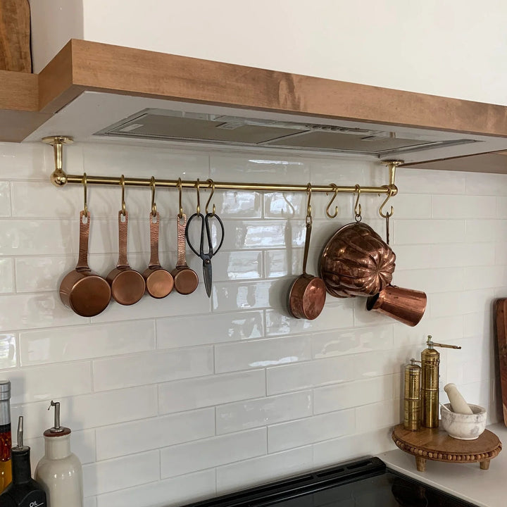 Unlacquered brass ceiling mounted pot rail with S-hooks holding copper pans